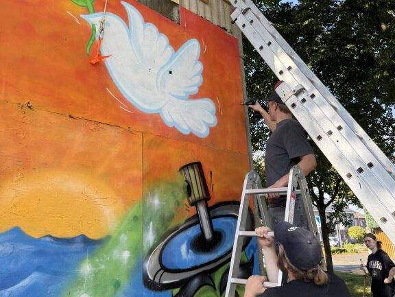 Pfadfinder montieren bemalte Holzplatten mit Taubenmotiv an der Fassade eines Glockenturms, eine Leiter steht am Turm